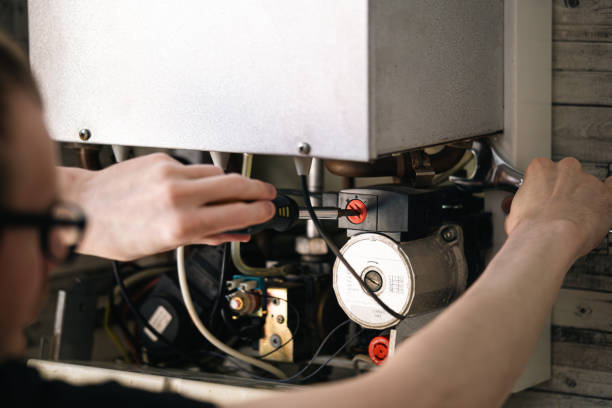 Technician performing maintenance on heating system, inspecting electrical components and wiring in the heating unit.